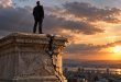Executivo sobre pedestal rachado ao pôr do sol